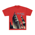 A red short-sleeve graphic t-shirt featuring a stylized art deco illustration of the New York City skyline, with 'THE STROKES' and 'NEW YORK' printed across the chest.