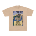 A beige crewneck t-shirt featuring a vintage-style concert poster graphic for 'The Strokes' 'Flushing Meadows Corona Park' on the front, displayed against a solid white background.