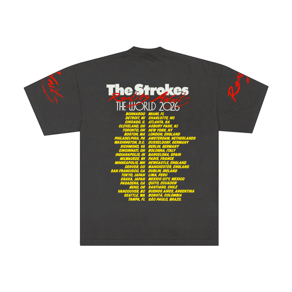 Dark grey t-shirt for the band The Strokes. Back of t-shirt features The Strokes Reality Awaits The World 2026 across the top with the 2026 tour itinerary in yellow down the back.