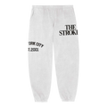 White fleece sweatpants with the text 'THE STROKES' printed on the left upper thigh and 'NEW YORK CITY EST. 2001' printed across the right thigh.