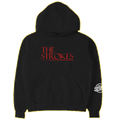 Black hoodie with 'The Strokes' text printed in red on the front across the chest and a white Strokes Chrome Logo on the left forearm. 